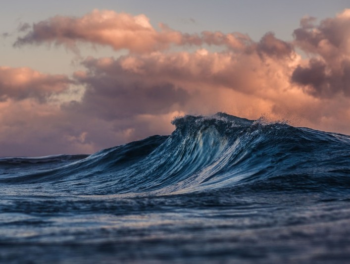 Large turquoise ocean wave cresting with white foam under a pastel sunset sky
